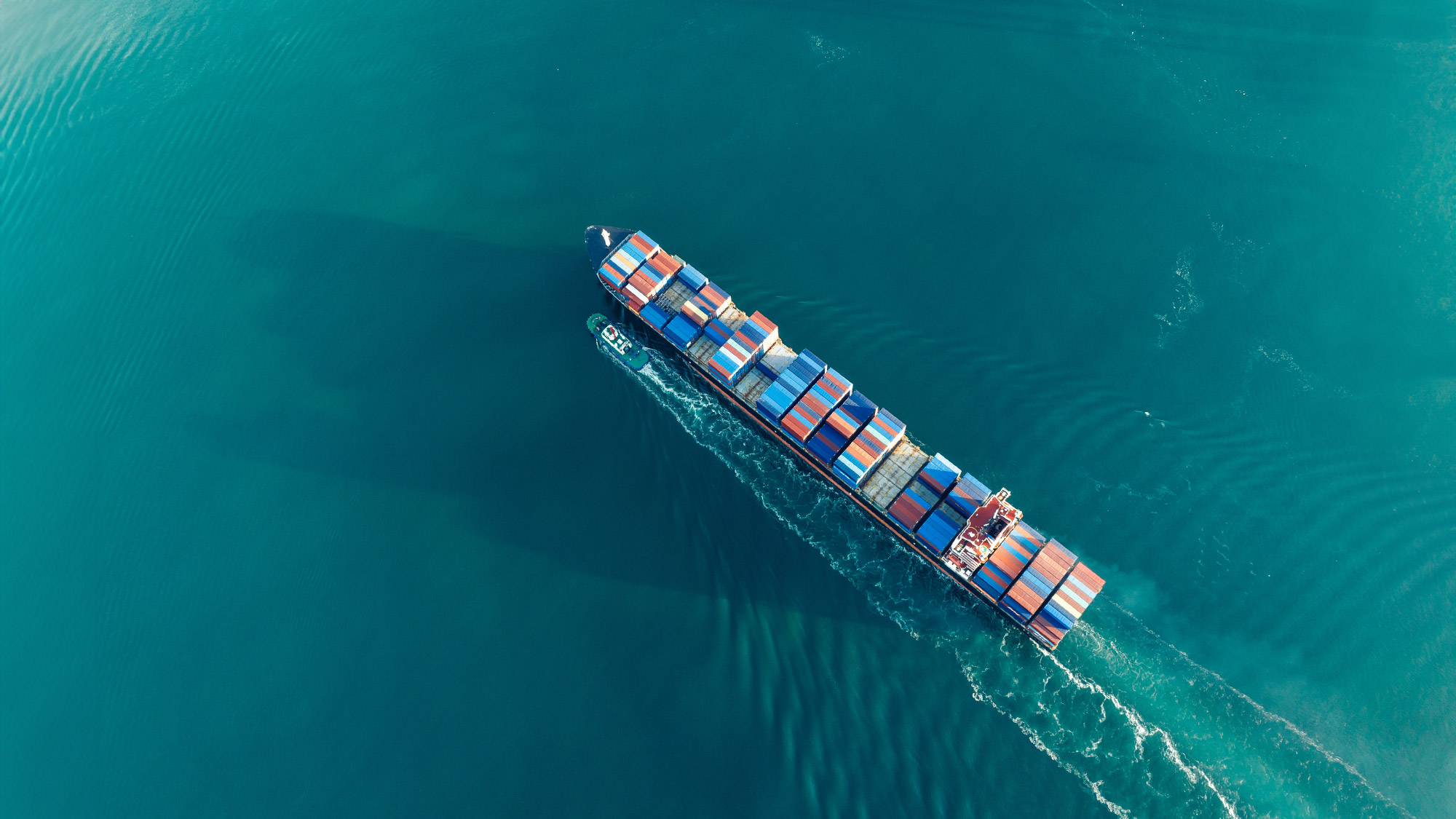 An top-down aerial view of a container ship in bright blue ocean water.