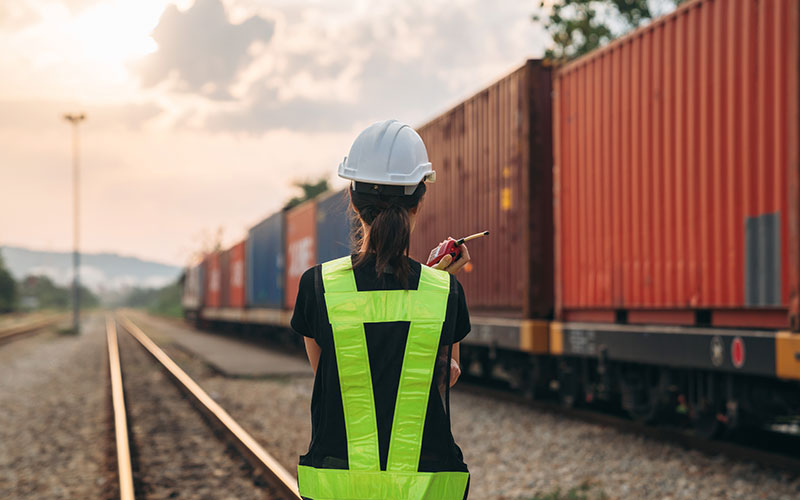 A female in safety equipment examines a train.