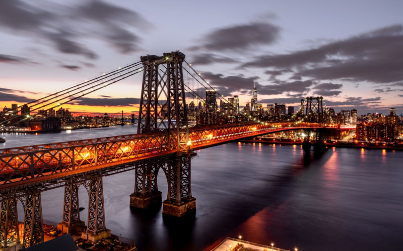 A bridge is lit up at night time in a large city.