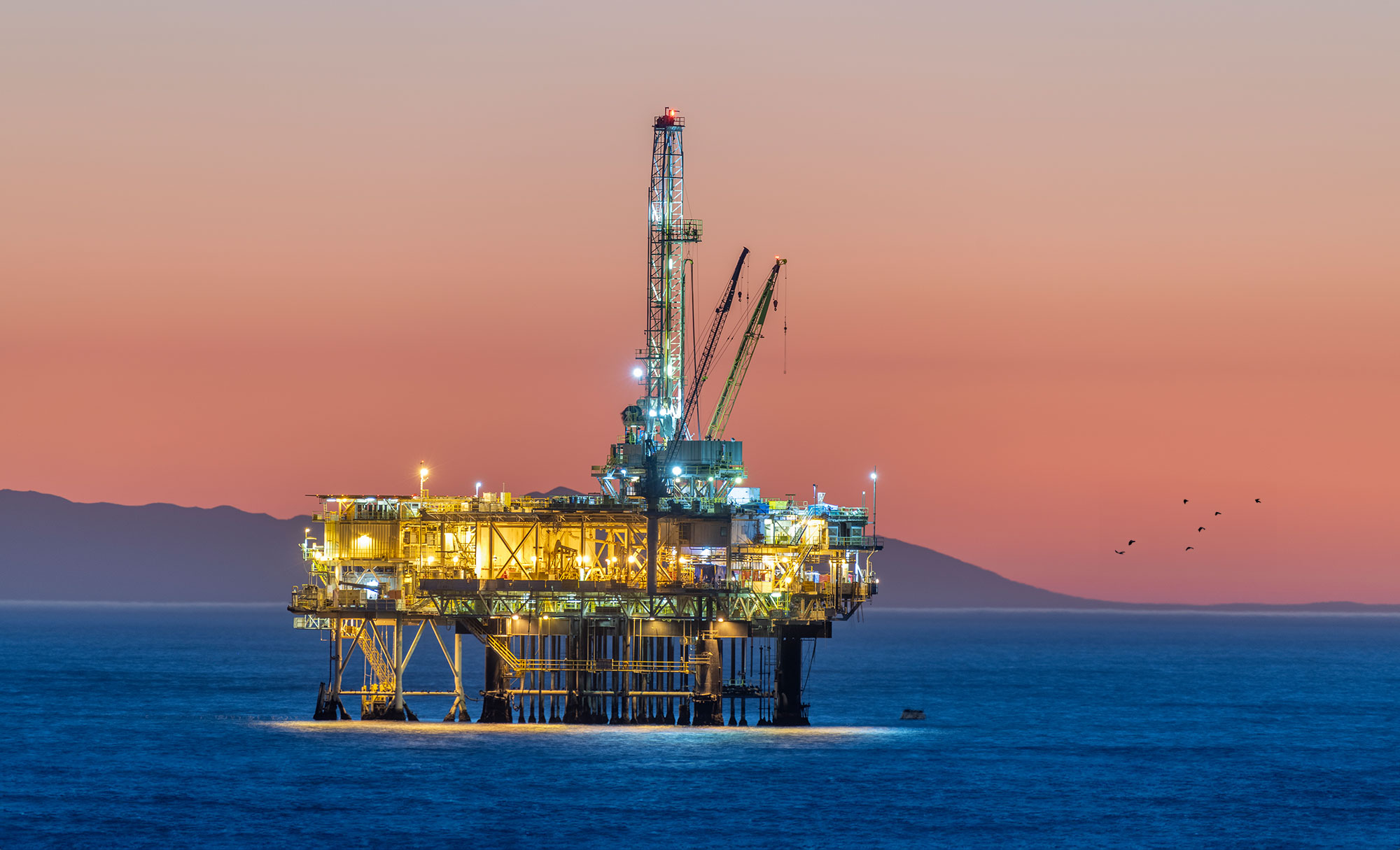 An oil rig stands in the sea at sunset.